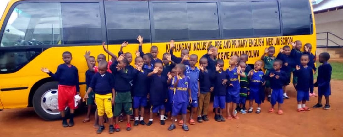 Das Bild zeigt Kinder vor ihrem neuen Schulbus in Tansania.