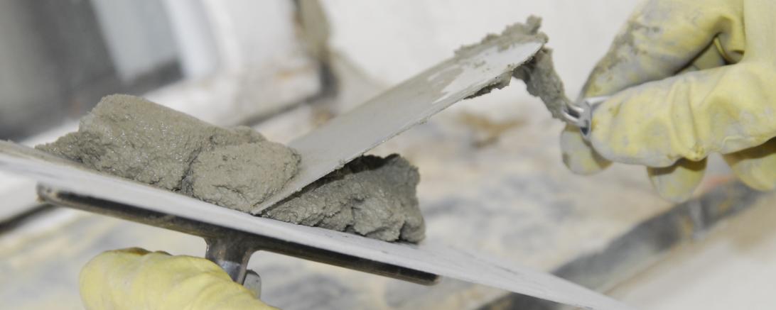 Zu sehen ist eine Maurerkelle, die von zwei Händen gehalten wird. 