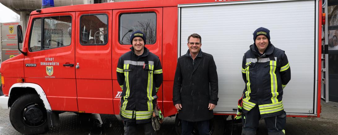 Zu sehen sind zwei Feuerwehrmänner und der Donauwörther Oberbürgermeister, welche vor einem Feuerwehr stehen.