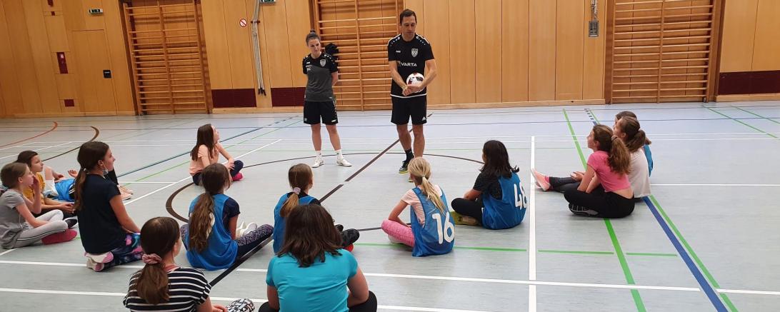 Zu sehen sind Markus und Sarah, wie sie den Schülerinnen etwas erklären. 