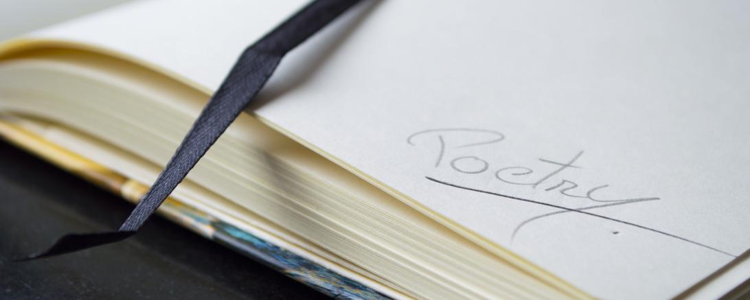 Zu sehen ist ein aufgeschlagenes Notizbuch, in dem das Wort "Poetry" geschrieben ist. 