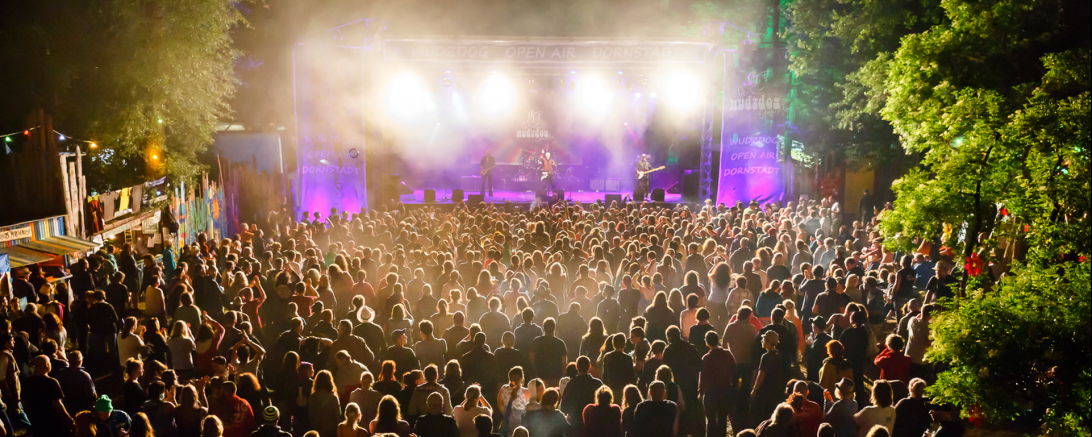 Zu sehen ist eine Bühne in hellem Licht mit vielen Zuschauern davor. 