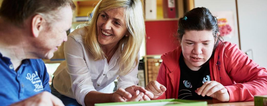 Das Bild zeigt eine Heilerziehungspflegerin mit ihren Patienten.