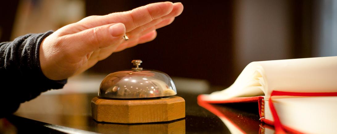 Hand auf Klingel an Hotelrezeption. 