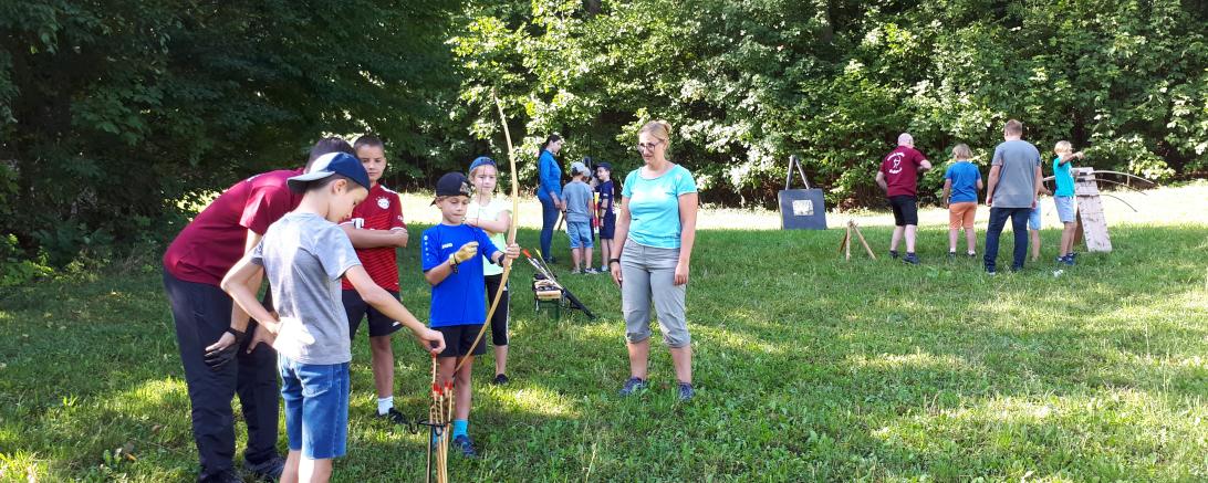 Das Bild zeigt die Kinder des Ferienprogramms beim Üben mit Pfeil und Bogen.