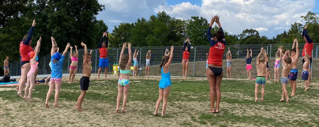 Das Bild zeigt die Ausbilder*innen und die Teilnehmer*innen des Kinderschwimmkurses bei einer Übung.