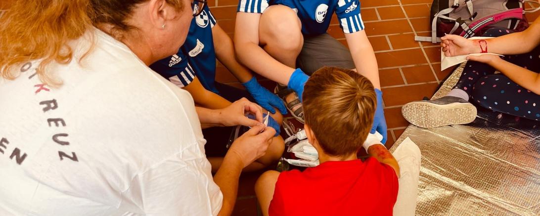 Das Bild zeigt eine Gruppe von Kindern, die sich beim Ferienprogramm die geschminkten Wunden gegenseitig verarzten.