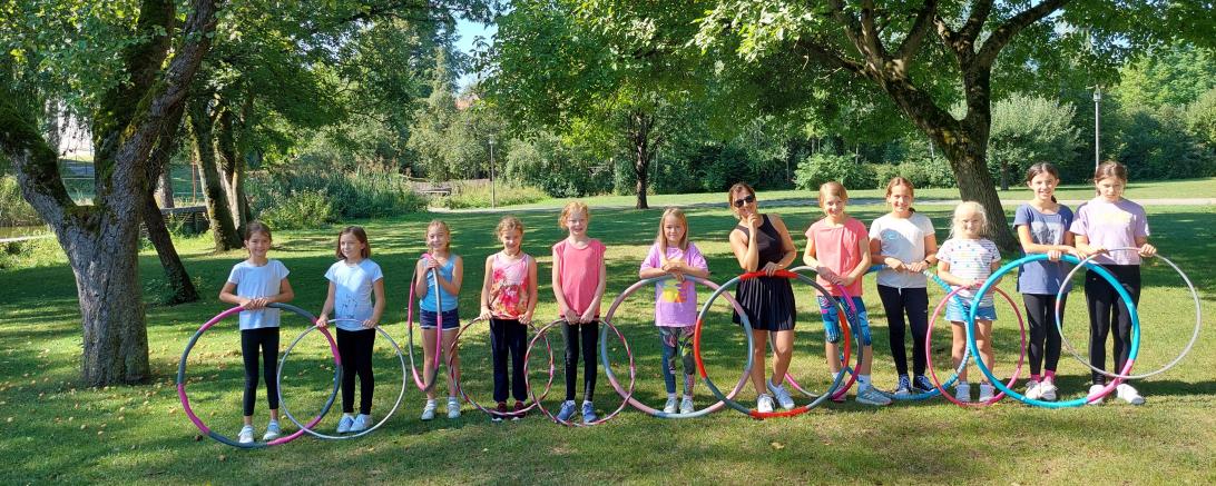 Das Bild zeigt die teilnehmenden Kinder des Ferienprogramms mit Hula Hoop im Stadtpark Rain.