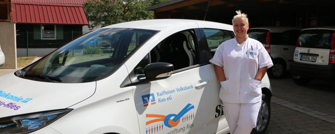 Das Bild zeigt Julia Budich vor einem Fahrzeug der Diakonie. 