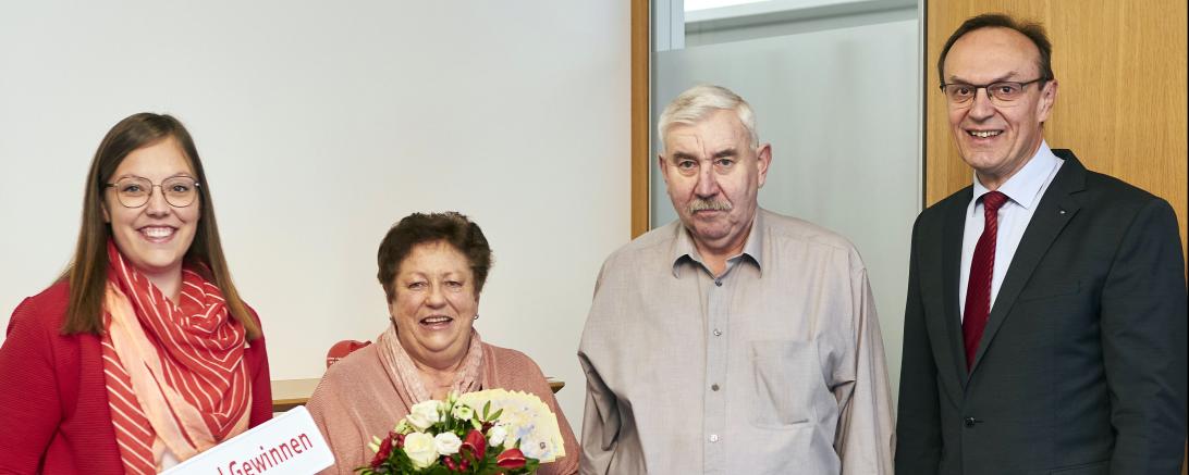 Auf dem Bild gratulieren in der Hauptstelle Kathrin Vetter und Sparkassendirektor Johann Natzer den beiden glücklichen Gewinnern Kundenberaterin mit einem Blumenstrauß