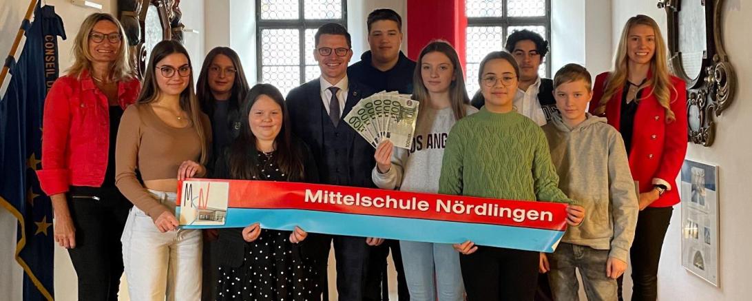 links Marga Riedelsheimer (Rektorin der Mittelschule Nördlingen), mittig Oberbürgermeister David Wittner, rechts Helena Ott (Leiterin Hauptverwaltung Stadt Nördlingen), umgeben von den Vertreterinnen und Vertreter der teilnehmenden Klassen der Mittelschule Nördlingen.