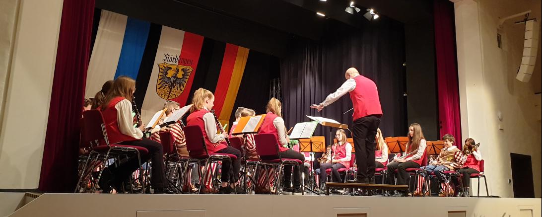  „In den Farben getrennt, in der Sache vereint!“ Das gilt auch für das äußere Erscheinungsbild des Doppel-Vororchesters. Die roten Westen für die Stadtkapelle sind pünktlich zum Konzert fertig geworden. So trugen die Musiker*innen dieses Ensembles schwarze Hose, weiße Bluse bzw. Hemd und rote Weste -  die Buben der Knabenkapelle ihre gewohnte schmucke Uniform. Auch Körner hatte eine rote Weste an.