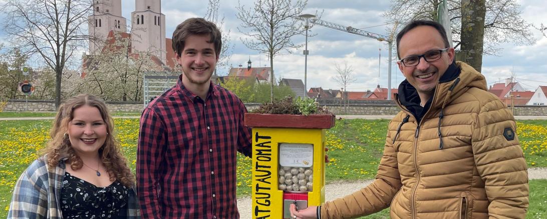 Sophie Fischer und Simon Strohofer zeigen Bürgermeister Martin Drexler den neuen Saatgutautomat am Johannisweiher. 