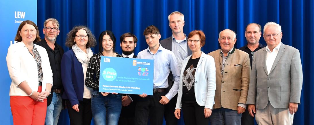 Preisübergabe Zukunftsheld*innen: Im Beisein der stellvertretenden Landrätin Claudia Marb (l.) und Wemdings zweiten Bürgermeister Johann Roßkopf (r.), übergab Walter Albrecht, Leiter Kommunalmanagement bei LEW (5.v.r.) Schülerinnen und Schülern sowie Vertretern der Anton-Jaumann-Realschule den symbolischen Scheck über 750 Euro für den 2.Platz beim 3malE-Nachhaltigkeitswettbewerb Zukunftsheld:innen. Personen von links nach rechts: Claudia Marb (stellvertretende Landrätin), Christian Quirrenbach (Projektbetre