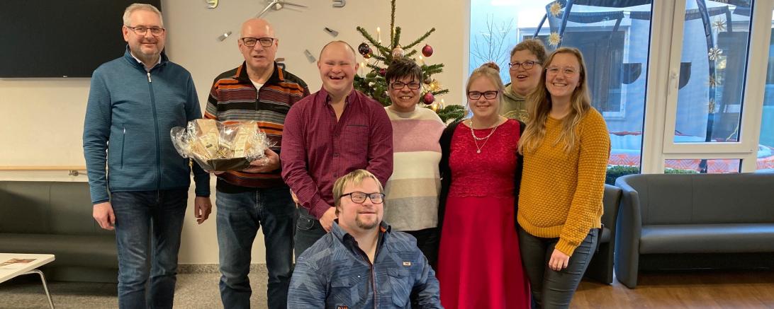 Das Bild zeigt einen Teil der fröhlichen Weihnachtsfans gemeinsam mit Standortleiter Thomas Mayer (ganz links) und Sozialdienstmitarbeiterin Laura Fischer (ganz rechts).