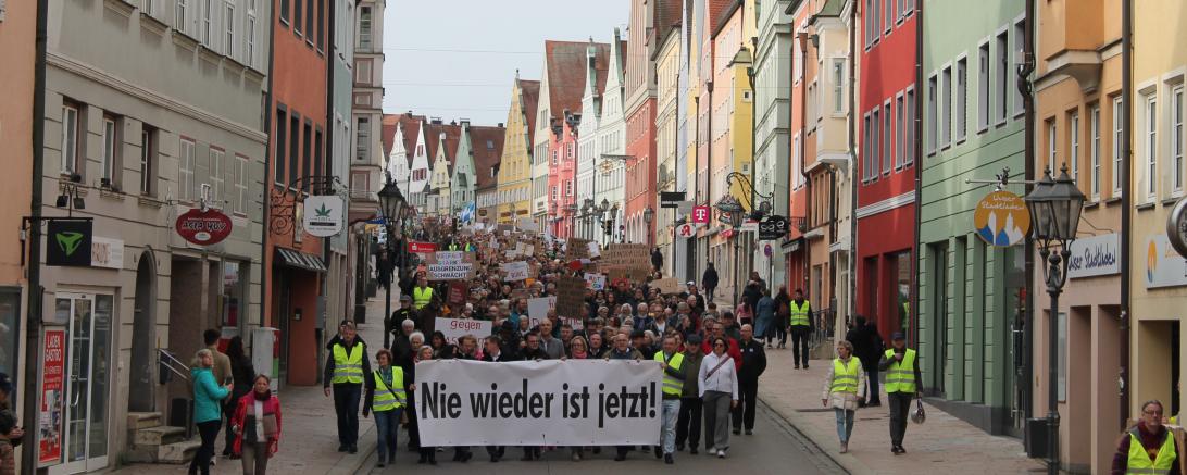 Das Bild zeigt die Demonstrant*innen in der Donauwörther Reichsstraße. Auf einem Banner steht: Nie wieder ist jetzt.
