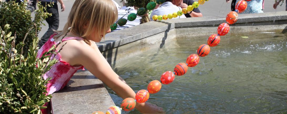 Auf dem Bild ist ein Kind an dem geschmückten Osterbrunnen zu sehen.
