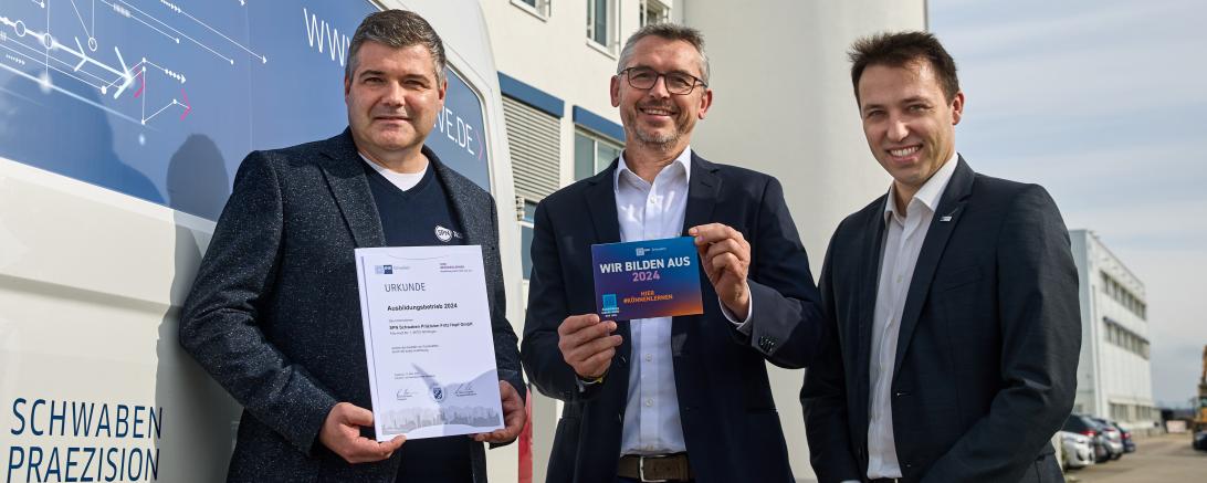 Jürgen Sieber (Verantwortlich für gewerbliche Ausbildung), Rainer Hertle (Techn. Geschäftsführer) und IHK Regionalgeschäftsführer Matthias Hausmann v.l. mit Urkunde und Aufkleber vor dem Firmengebäude von SPN, Schwaben Präzision in Nördlingen