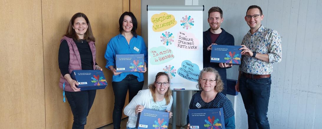 4 Personen Hinten die Stehen, Zwei Personen vorne die Knieen. Alle Schauen in die Kamera und Lächeln.