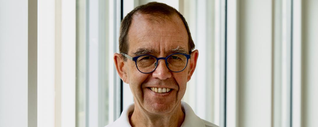 Mann mit weißem Poloshirt  der die Arme verschränkt 