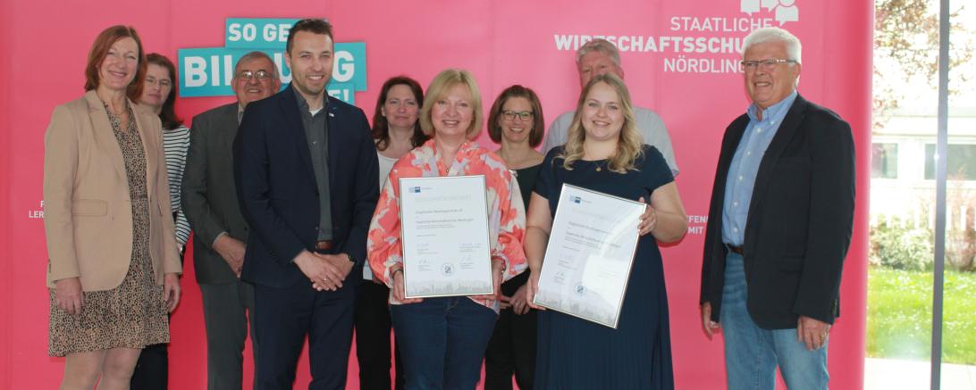 Menschen die vor einer werbewand stehen und zwei Zertifikate in der Hand halten