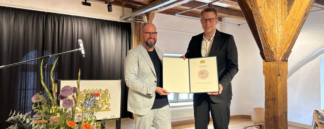 Staatsminister Markus Blume überreicht die Urkunde "Bayerns Buchhandlung des Jahres 2023" an Matthis Lehmann. 
