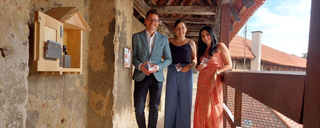 Oberbürgermeister David Wittner mit Sarah Fackler und Sarah Wörz, die für Layout und Konzeption der neuen Kinderlinie verantwortlich waren, an den neuen Stempelhäuschen auf der Stadtmauer.