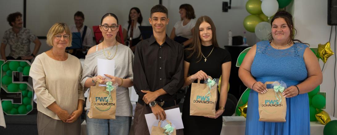 Neben der Schulleiterin Gabriele Braun von links nach rechts: Victoria Lohwasser, Matej Dushkov, Romy Elsässer, Louisa Förg Im Hintergrund die Lehrerband mit Bastian Offinger, Ivo Schwalbe, Julia Ratzek und Kristina Unterweger