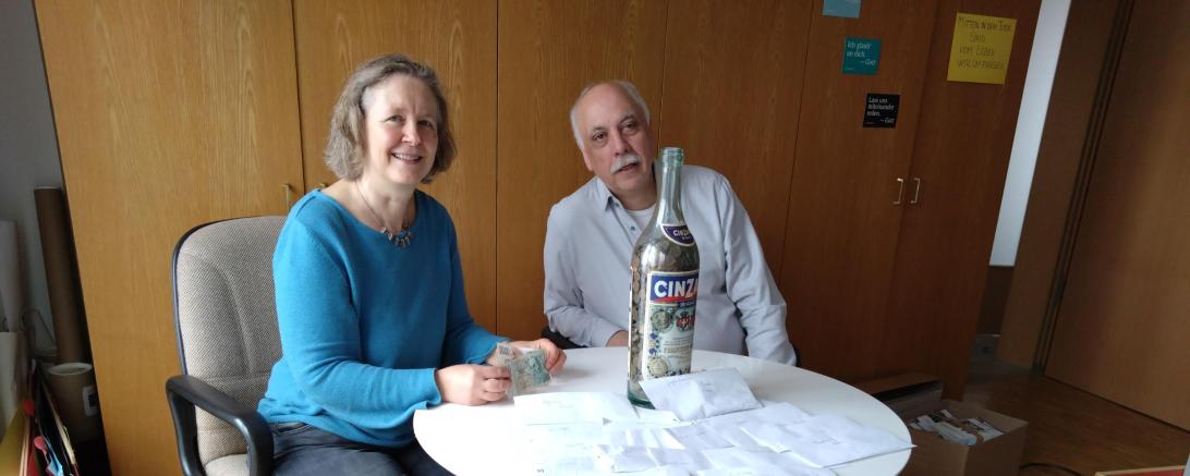 zwei Menschen sitzen an einem Runden Tisch, davor ein Hund