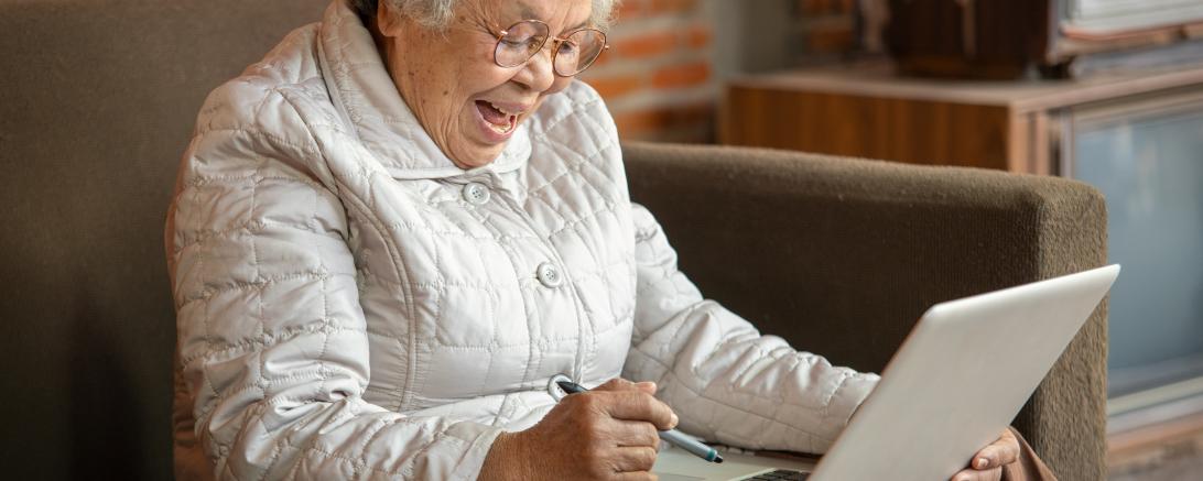 Auf dem Foto ist eine ältere Frau mit einem Laptop zu sehen.