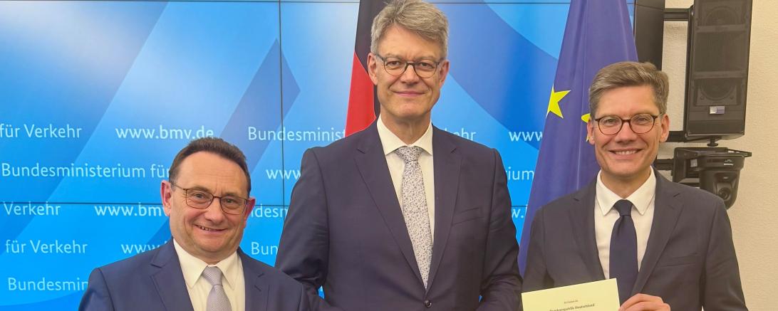 Ulrich Lange (l.) erhält die Urkunde vom neuen Verkehrsminister Patrick Schnieder (M.).