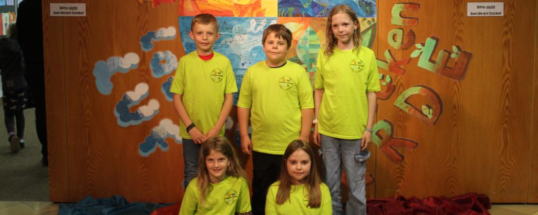 Amerdinger Grundschule in den neuen Schul-Shirts vor dem Wandgemälde im Eingangsbereich.