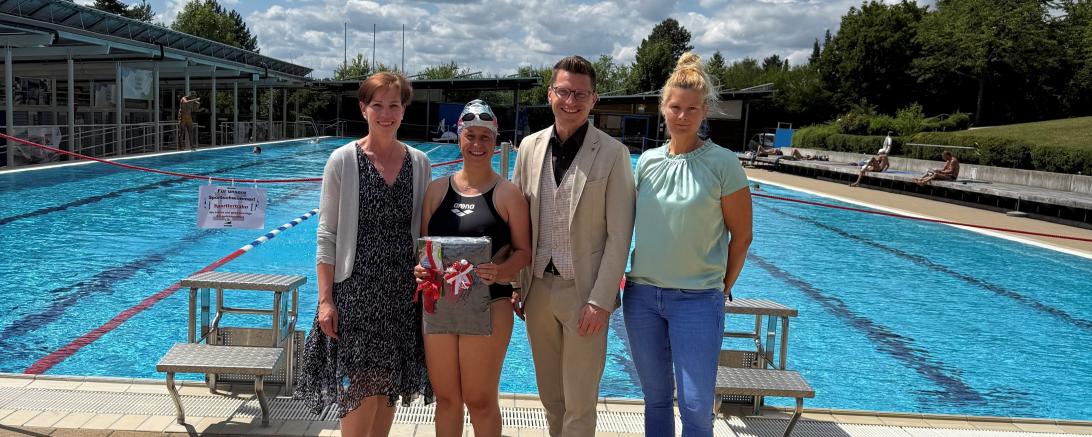 Oberbürgermeister David Wittner (2. v. r.), Simone Leidel (links, stellvertretende Leitung des Sachgebiets Liegenschaften, Schulen, Sport) und Nicole Hofmann (rechts, stellvertretende Betriebsleiterin der Bäder) gratulieren der 50.000. Besucherin Lena Steinle (2. v. l.).