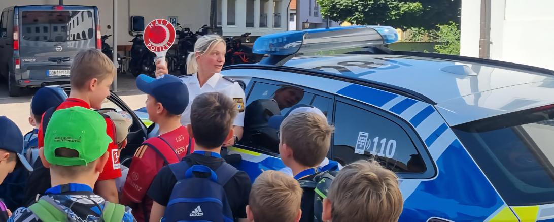 Teilnehmende Kinder und Polizistin Frau Stephanie Mergel vor einem Dienstwagen.