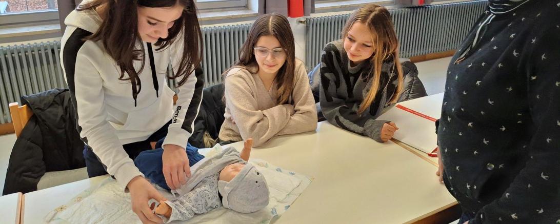 Das Bild zeigt, wie die Teilnehmenden das Wickeln eines Kleinkindes unter Anleitung der Facherzieherin Stefanie Baumgärtel trainieren. 