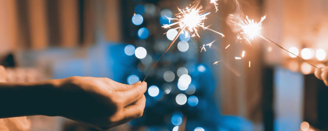 Hände mit Wunderkerzen, im Hintergrund ein Weihnachtsbaum. 