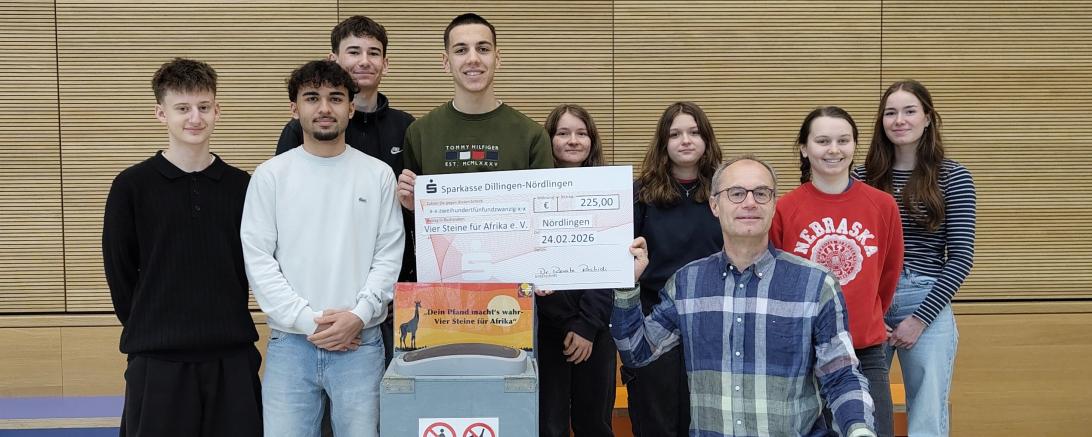 Das P‑Seminar „Klimaschule“ übergibt 225 Euro aus der neu aufgestellten Pfandspendenbox an Martin Stumpf (Vier Steine für Afrika e. V.).