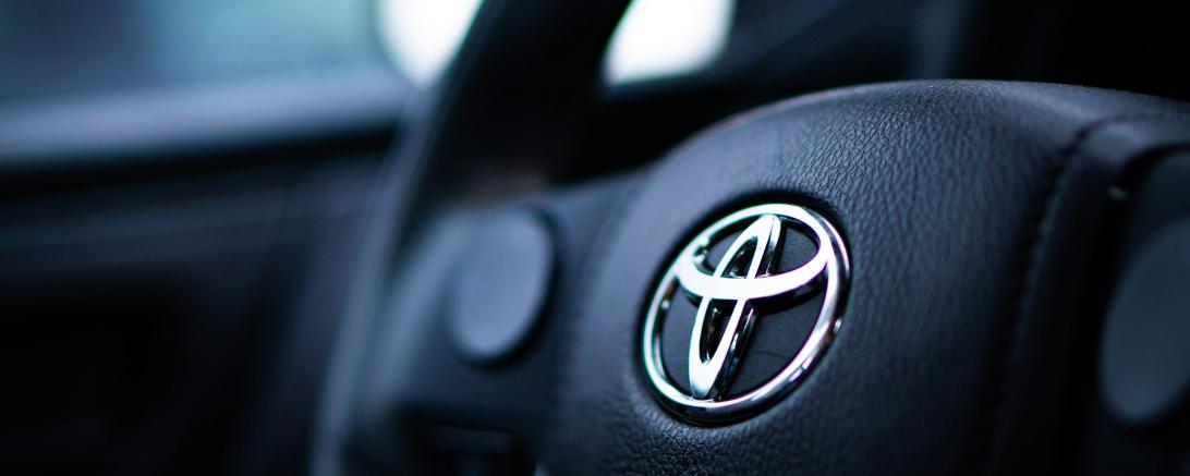 Schwarzes Lenkrad mit silbernem Toyota-Logo aus Metall.