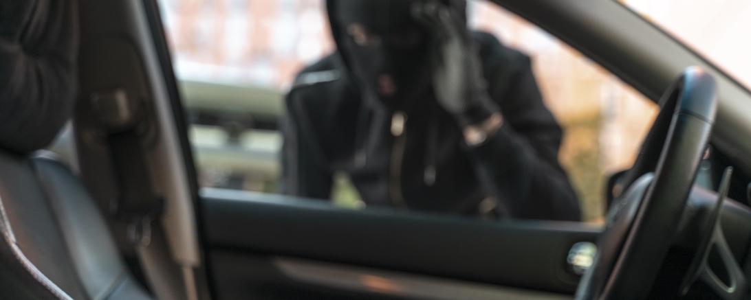 Symbolbild eines maskierten Mannes an einem Auto. Im Vordergrund ein Geldbeutel. 