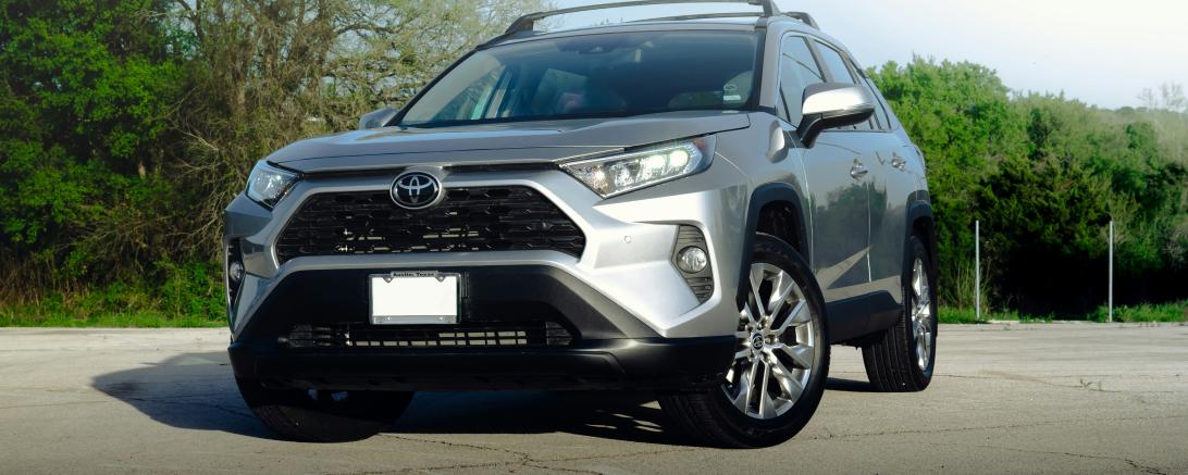 Silberner Toyota RAV4 steht auf einem asphaltierten Platz vor einem Wald.
