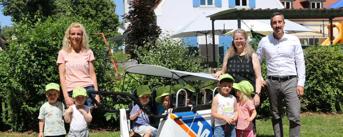 Simon Rupprecht von der Raiffeisen-Volksbank Ries übergibt den Kinderbus an die Krippenerzieherinnen Svenja und Veronika im Gemeinde-Kindergarten Otting.