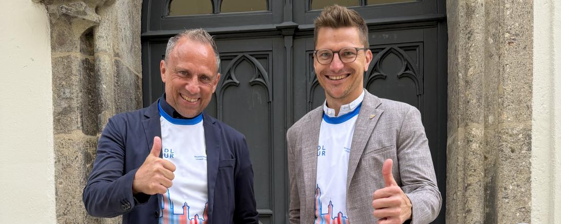 Bayerns Umweltminister Thorsten Glauber und Oberbürgermeister David Wittner präsentieren das Sondertrikot für den ersten BR-Radltag der BR-Radltour 2026 in Nördlingen und freuen sich auf den Auftakt der Tour am 2. August.