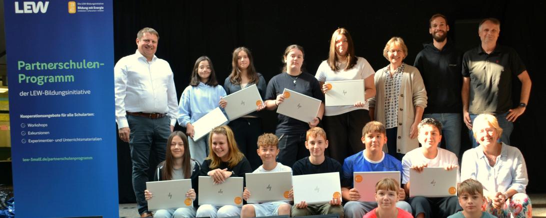 Michael Smischek (obere Reihe links), Wolfgang Schwarz, Mario Steixner, Heike Ritzka (obere Reihe von rechts) und Bärbel Stahl (mittlere Reihe rechts) freuen sich mit Schülerinnen und Schülern der Klasse 7a über die von der LEW gesponserten Laptops und Monitore. 