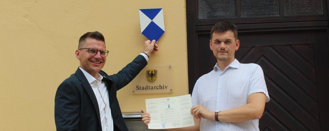 Nördlingens Oberbürgermeister David Wittner (l.) und Stadtarchivar Dr. Johannes Moosdiele-Hitzler präsentieren das Schutzschild und die Urkunde.