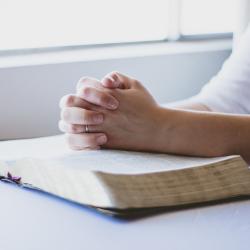 Frau hat ihre Hände gefaltet und betet auf einer Bibel