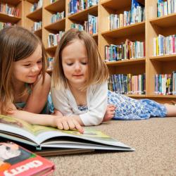 Das Bild zeigt zwei Kinder in der Bibliothek beim Lesen. 