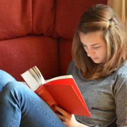 Junge Frau liegt auf rotem Sofa und liest ein rotes Buch