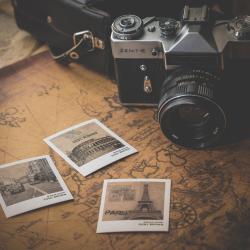 Auf dem Bild sieht man eine alte Kamera. Vor ihr liegen Polaroid Bilder von Reisen.