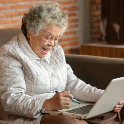 Auf dem Foto ist eine ältere Frau mit einem Laptop zu sehen.